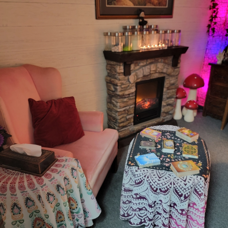 Soft pink client chair beside a stone fireplace and tarot table in The Zen Shop’s Reading Parlour