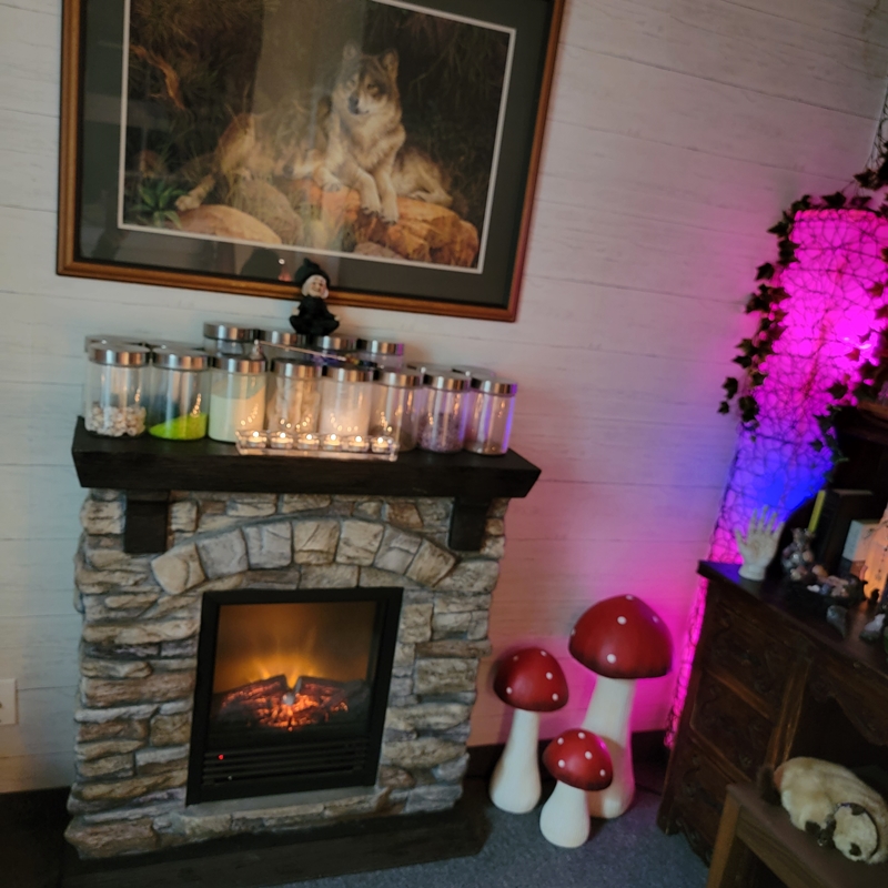 Faux stone fireplace surrounded by a crystal display, glowing mushrooms, and spiritual decor in The Zen Shop’s Reading Parlour