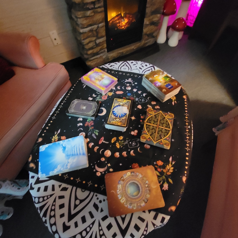 Assorted tarot and oracle decks arranged on a mystical cloth-covered table between two chairs in The Zen Shop’s Reading Parlour