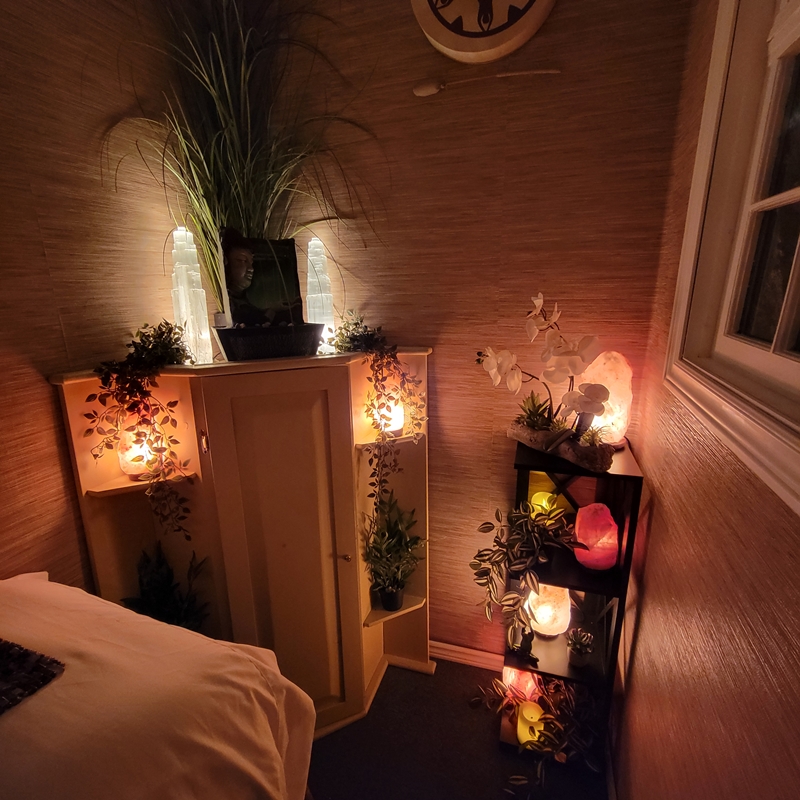 Head of the Reiki bed in The Zen Shop Healing Room with corner cabinet, glowing Himalayan salt lamps, indoor plants, water fountain, and crystal shelf