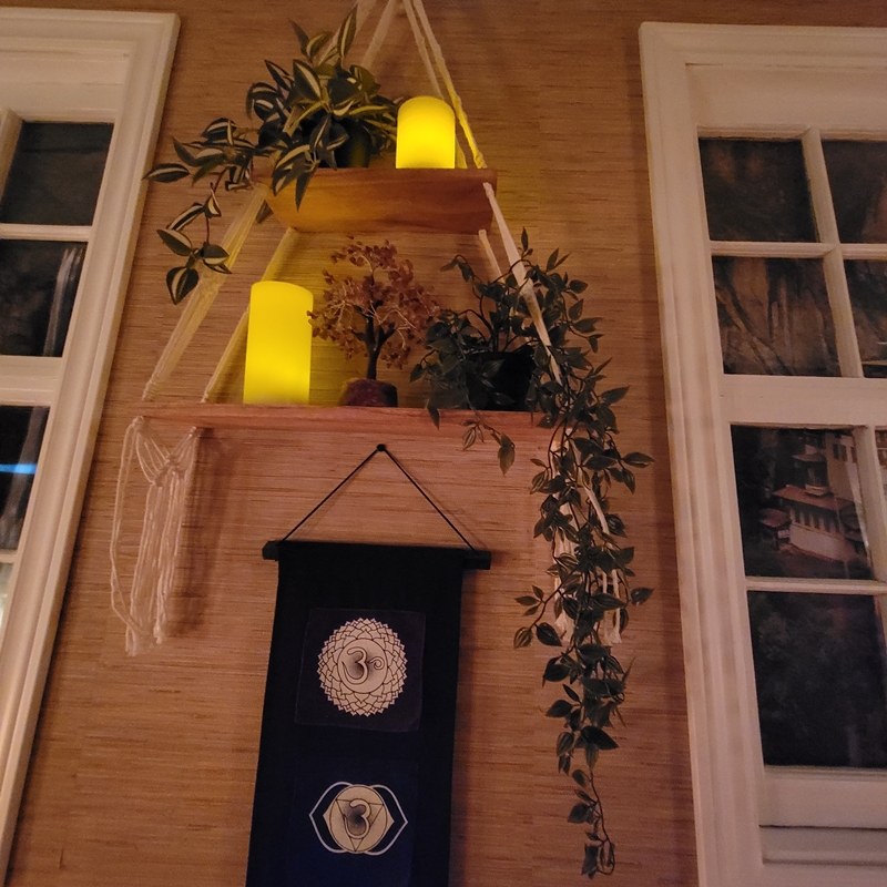 Floating triangular wooden shelf in The Zen Shop Healing Room with flameless candles, leafy vines, gemstone tree, and a chakra wall hanging below