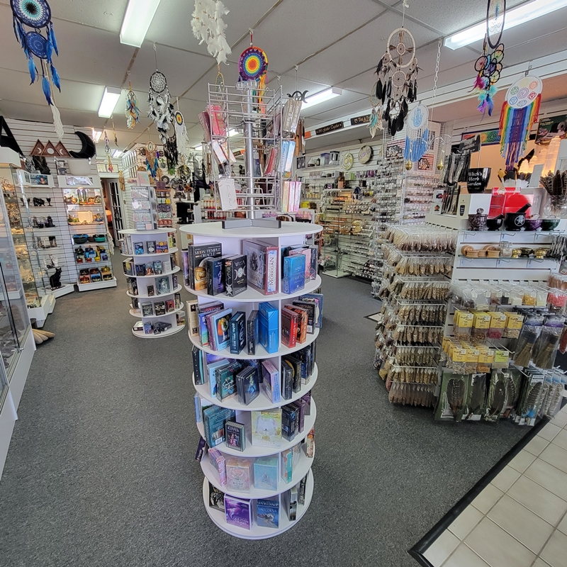 Mid-store view at The Zen Shop Oshawa looking into the centre aisle, featuring rotating displays of tarot and oracle cards, Hoodoo and resin incense, dried herbs, and metaphysical supplies.