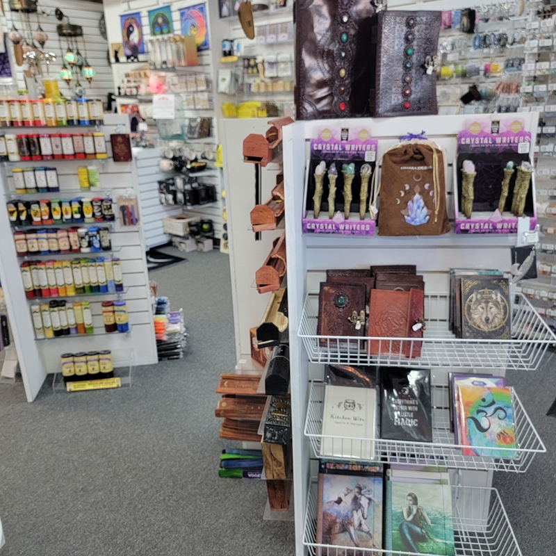 Centre display at The Zen Shop Oshawa featuring leather-bound journals, crystal writer pens, hardcover notebooks, and themed writing accessories. Spiritual intention candles and metaphysical supplies are visible in the background.
