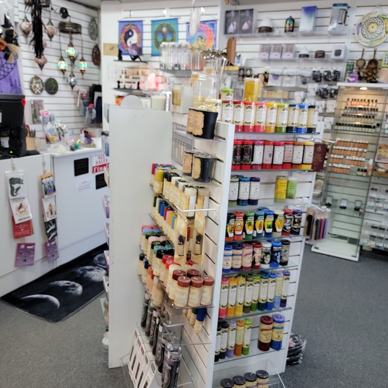 Back centre view of The Zen Shop Oshawa showcasing a vibrant display of spell candles and ritual candles in a wide variety of colours, sizes, and magical intentions. The checkout counter, spiritual wall décor, and apothecary shelves can be seen in the background.