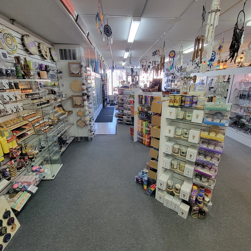 Back-of-store view at The Zen Shop Oshawa highlighting gemstone jar candles, votive candles, and Shaman candles, with wellness and self-care products on the left and spiritual candles, incense, and crystal cabinets lining the aisle toward the front entrance.