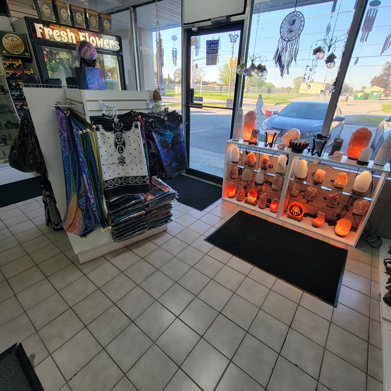 Front door area of The Zen Shop Oshawa featuring glowing Himalayan salt lamps, altar cloths, and mystical tapestries. Suncatchers and dreamcatchers hang in the window above the lamps, filling the entrance with rainbow reflections and positive energy.