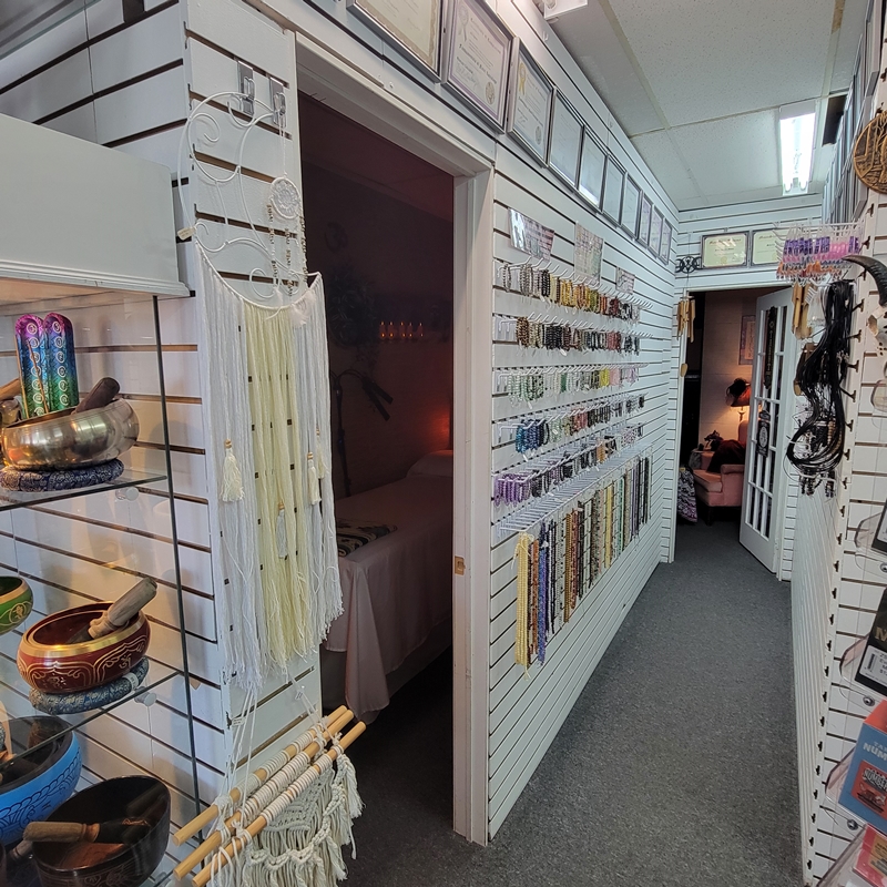 Back hallway of The Zen Shop Oshawa featuring a vibrant wall display of crystal bracelets, beads, and beading supplies. Above, framed credentials and certifications from the shop’s professional staff are proudly displayed. The hallway leads to the Healing Room and Reading Parlour entrances.