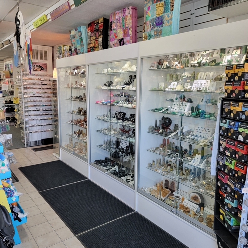 North wall view from just inside the front entrance of The Zen Shop Oshawa, showcasing Buddha Teas, crystal specimen cabinets, tumbled stone bins, and stacked patchwork meditation cushions.